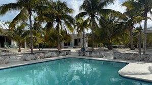 A swimming pool with palm trees and a building in the background. - Cottage 6 - Charming 1-bedroom cottage-pool-tennis-walk to beach in Sandy Point (Sandy Point)
