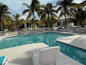 A swimming pool with lounge chairs, surrounded by palm trees and a building with a white facade.