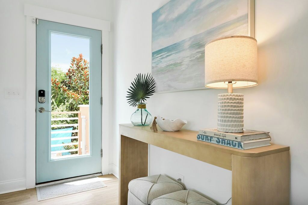 A modern entryway with a light blue door, a console table with a lamp, a framed artwork, and a small potted plant.