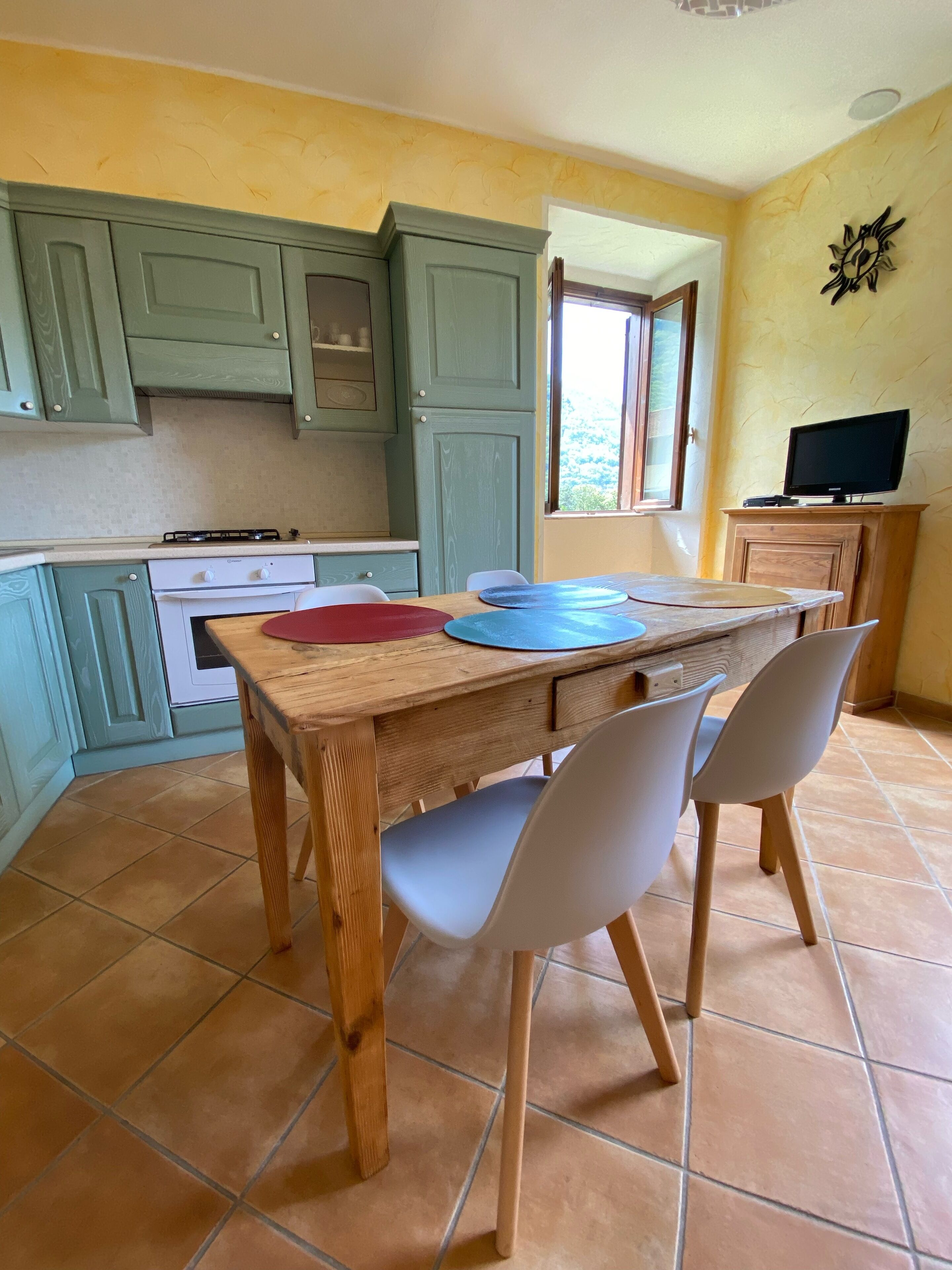A kitchen with green cabinets, a wooden table, and two white chairs.