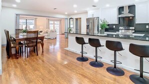 A modern kitchen with a central island, bar stools, and a dining area with a wooden table and chairs. - The Seminole Heights Suncatcher - Pool & Basketball (Tampa)
