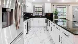 A modern kitchen with white cabinetry, a stainless steel refrigerator, and a marble floor. - The Seminole Heights Suncatcher - Pool & Basketball (Tampa)