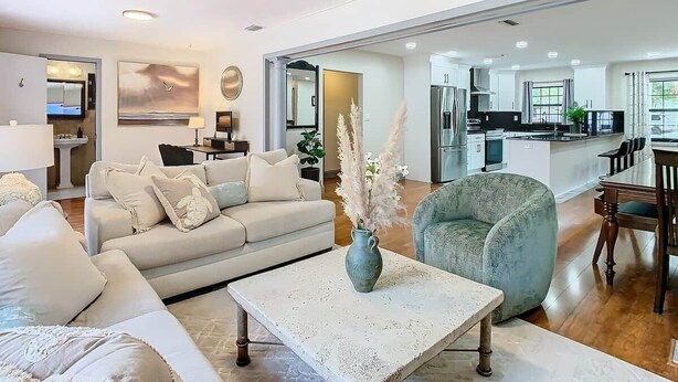 A modern living room with a sofa, armchair, coffee table, and a dining area with chairs. - The Seminole Heights Suncatcher - Pool & Basketball (Tampa)