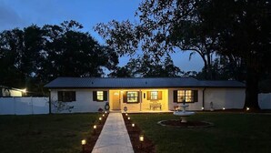 A house with a pathway leading to the front door, surrounded by trees and a well-maintained lawn. - The Seminole Heights Suncatcher - Pool & Basketball (Tampa)