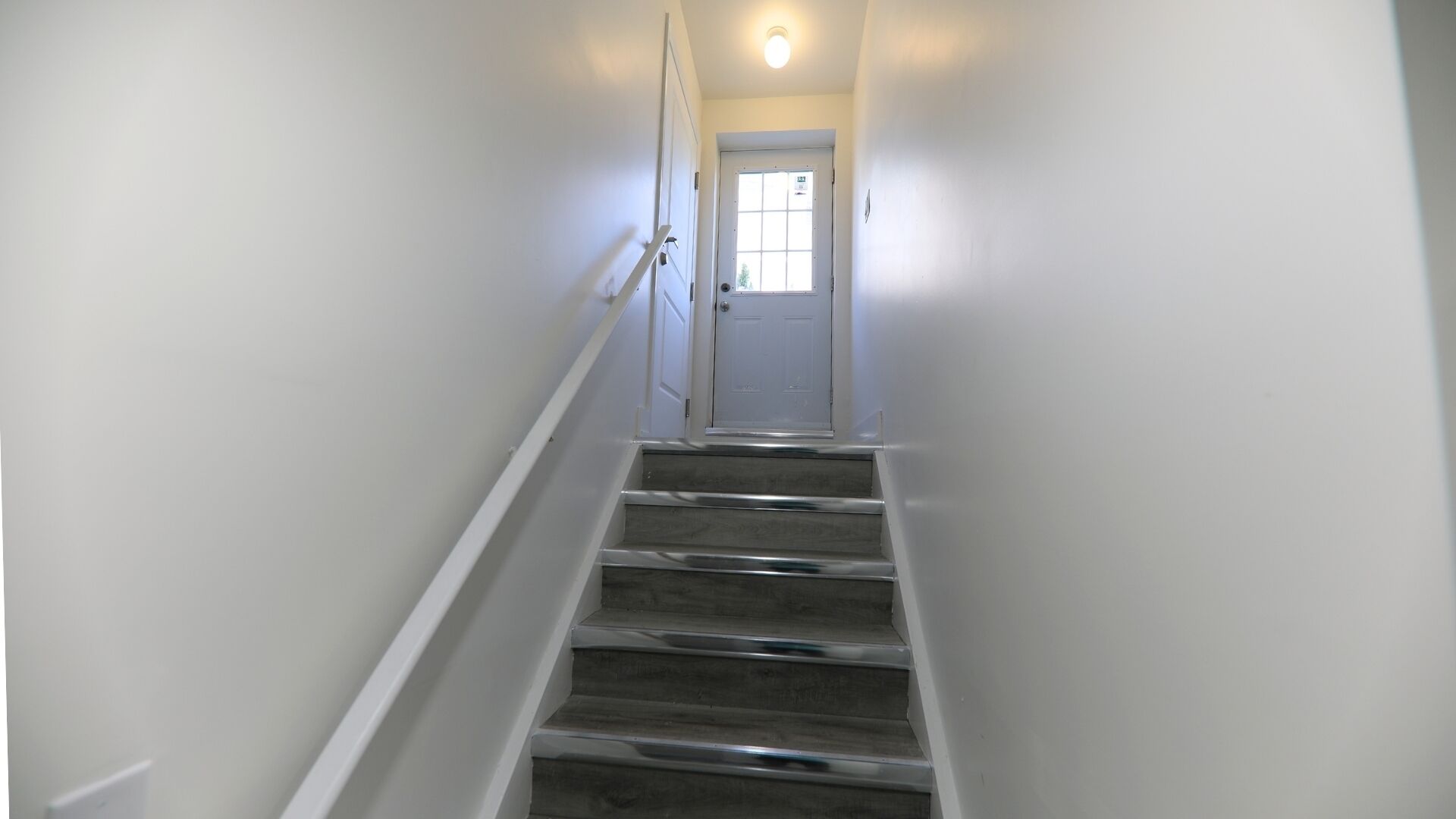 A narrow, well-lit stairway leading to a door with a frosted glass panel.