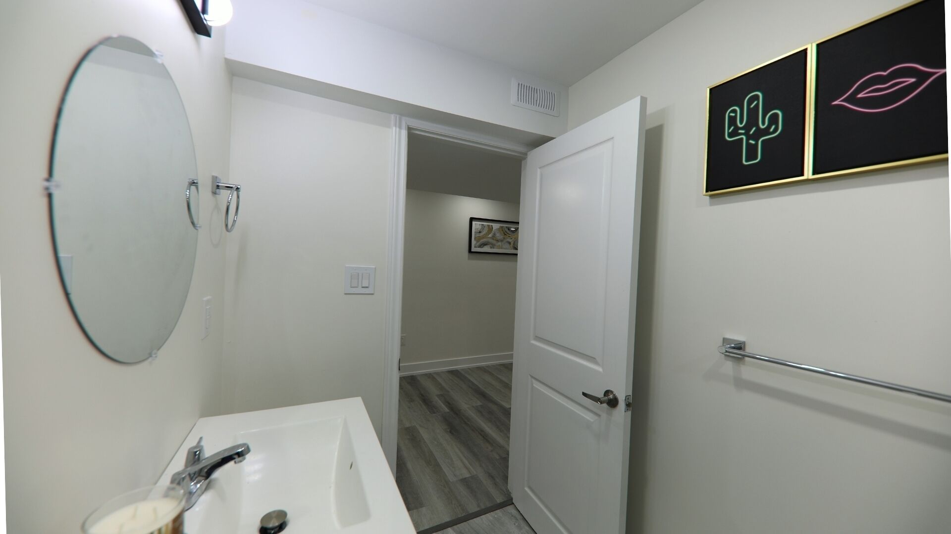 A bathroom with a white sink, mirror, and door. There are two framed pictures on the wall.