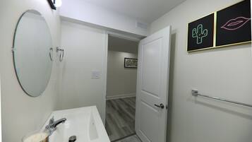 A bathroom with a white sink, mirror, and door. There are two framed pictures on the wall.