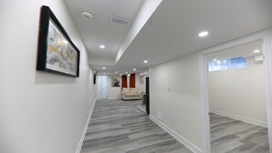 Un couloir moderne avec un plancher en bois gris, des murs blancs et un éclairage encastré.
