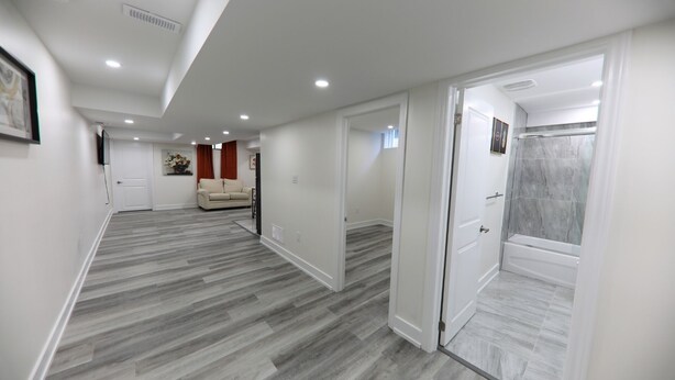 Un hall d’entrée spacieux aux couleurs neutres, avec un canapé beige et un espace douche doté d’une porte en verre.