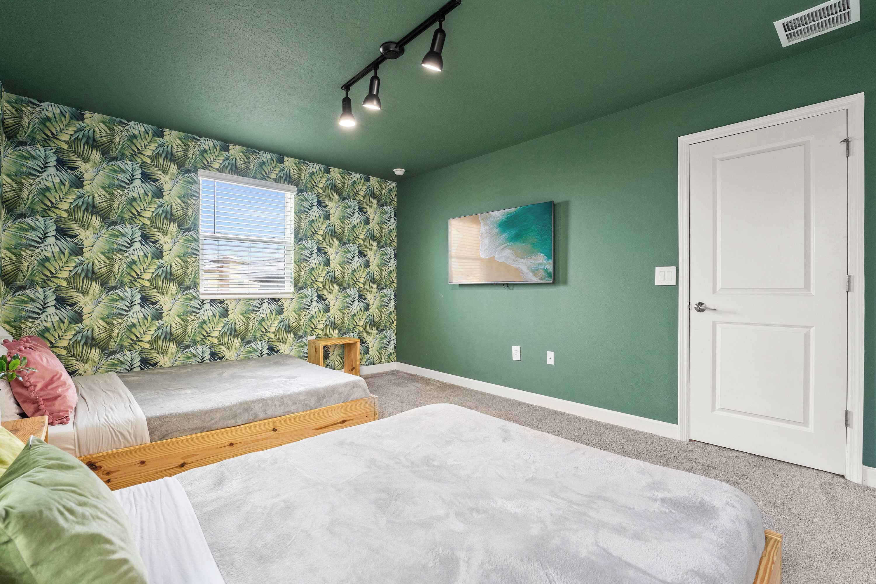 A room with two beds, a window with blinds, a painting, and a door.