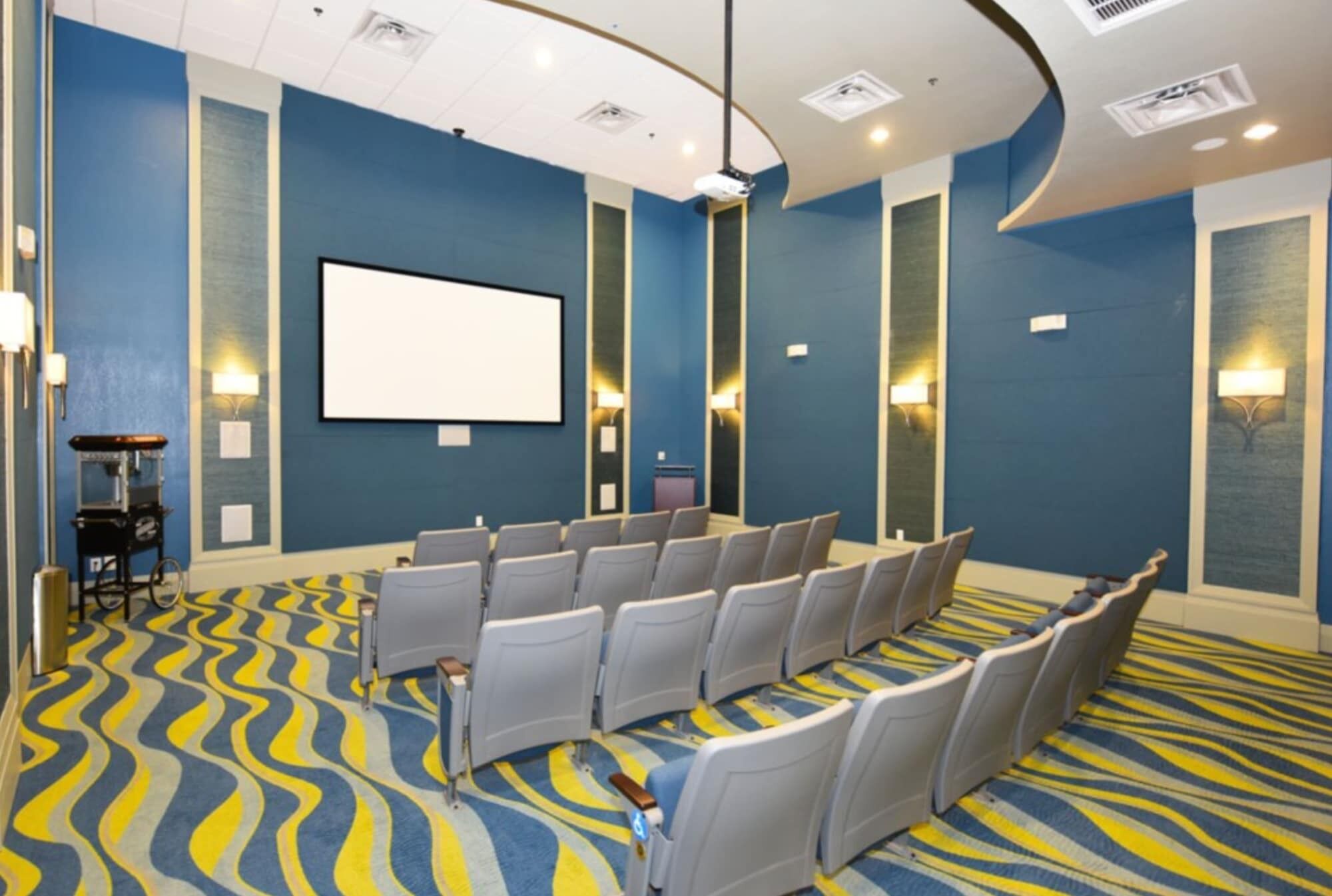A conference room with rows of chairs, a large screen, and a patterned carpet.
