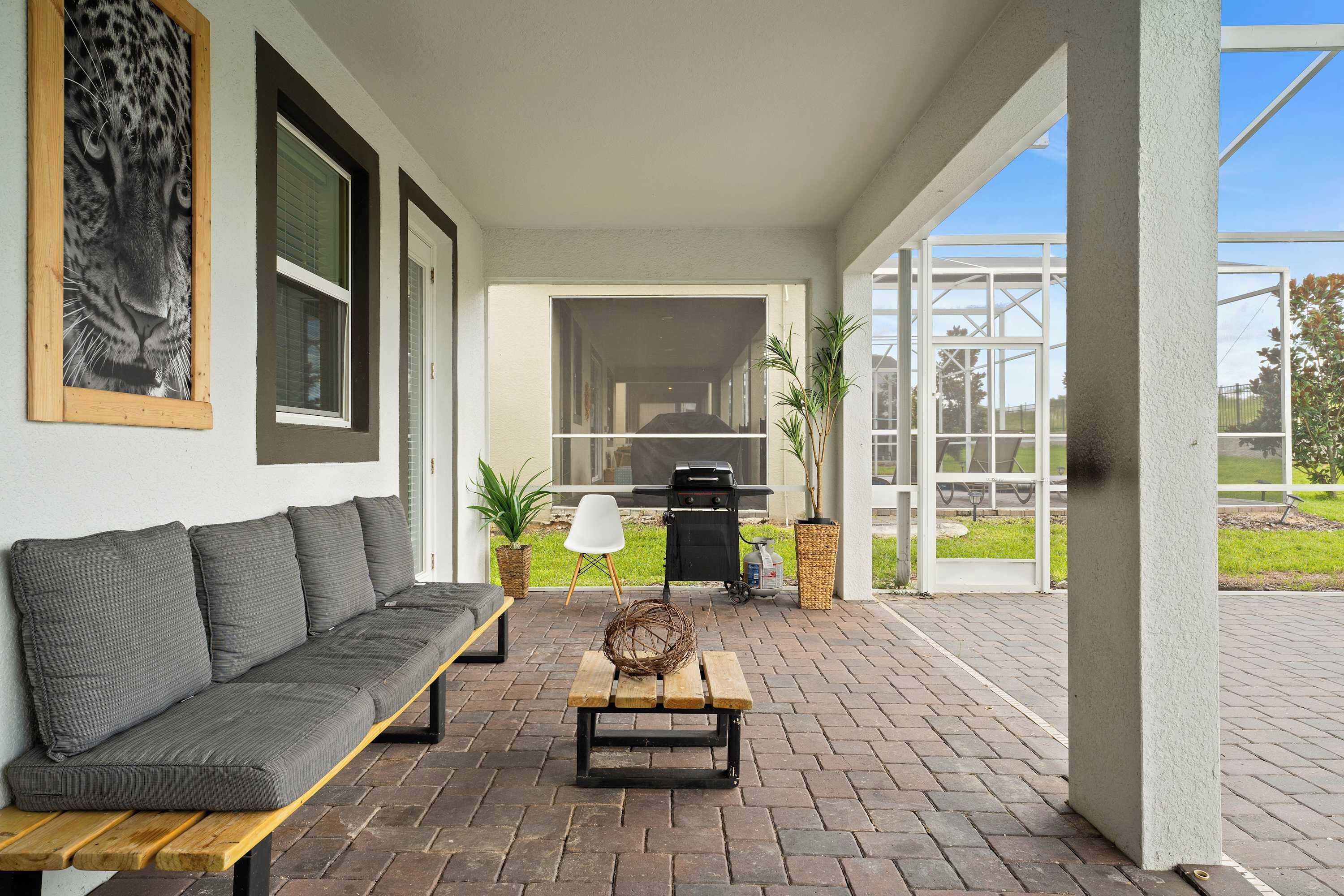 A covered patio area with a grey sofa, a wooden bench, and a decorative basket.