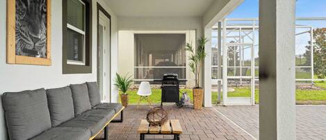 A covered patio area with a grey sofa, a wooden bench, and a decorative basket.