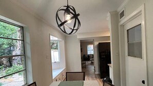 Un coin repas avec une table dressée pour quatre personnes, un luminaire suspendu et une vue sur l’extérieur grâce à de grandes fenêtres.