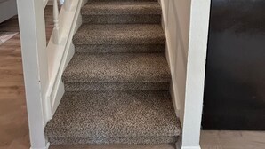 Un escalier recouvert de moquette, avec des rampes blanches, mène à une porte.