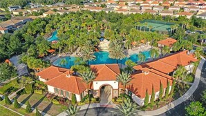 An aerial view of a residential area with a central swimming pool, surrounded by palm trees and houses with red-tiled roofs. - Solterra Bliss - Resort Stay for 13 w/ Pool, Hot Tub & Game Room (Davenport)