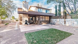 Une maison à deux étages dotée d’un patio couvert, de murs en pierre et d’une cour gazonnée.