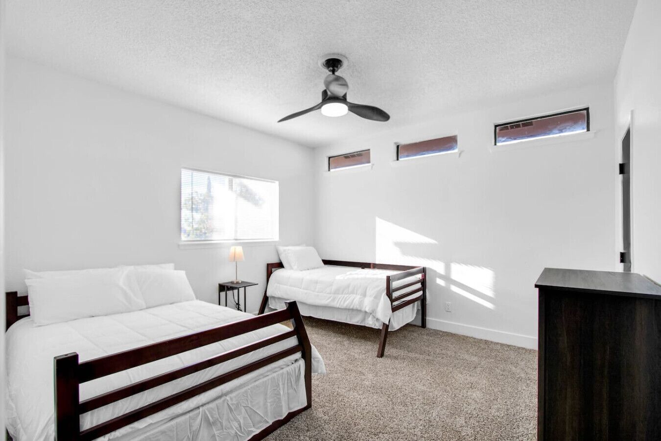 A bedroom with two beds, a ceiling fan, a window, and a small desk.
