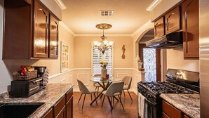 A kitchen with wooden cabinets, a stove, a dining table with chairs, and a chandelier.