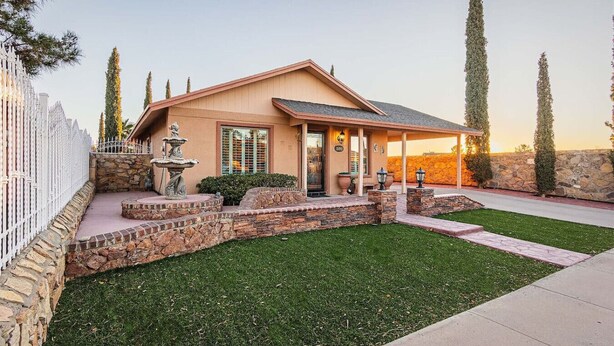 A single-story house with a stone facade, a front porch, and a small fountain.