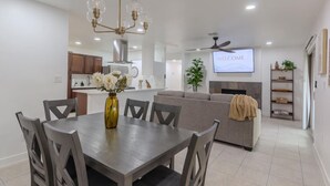 A modern living room with a grey sofa, a dining table with chairs, a chandelier, a TV screen displaying "WELCOME", and a ceiling fan. - Family home w/outdoor playground (El Paso)