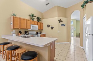 A kitchen with wooden cabinets, a white microwave, a sink, and a bar area with stools.