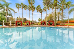 A swimming pool with red gazebos, surrounded by palm trees and a clear sky.