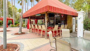 An outdoor patio area with a red-striped roof, several tables and chairs, and a food service counter. - Tropical Oasis on Hypolita (Davenport)