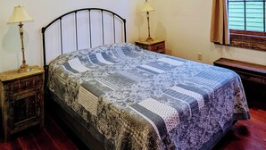 A bedroom with a bed, two bedside tables, a ceiling fan, a window with curtains, and wooden flooring.