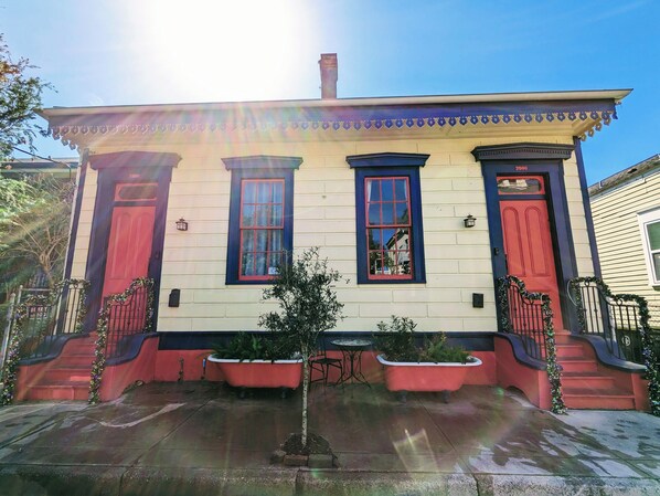 A two-story building with a red door, a window with a red frame, and a small tree in the front yard. - Historic charm & modern comfort near Frenchmen St! (New Orleans)