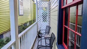 A covered outdoor balcony with a white railing, a small table, and two chairs.