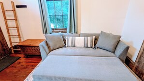 A cozy room with a large grey sofa, a wooden ladder, and a window with curtains.