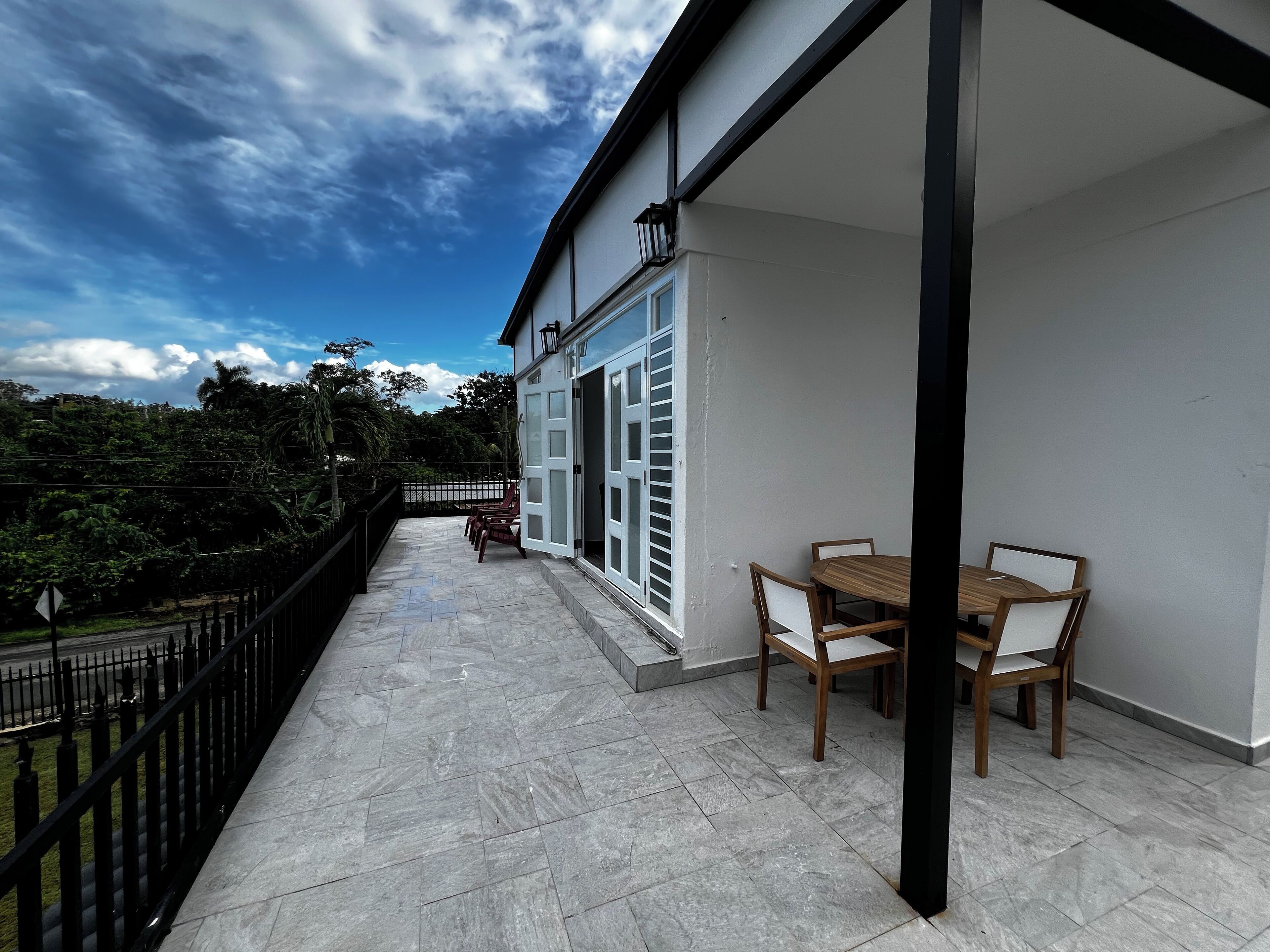 A balcony with a table and chairs, a railing, and a view of greenery and trees.