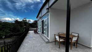 A balcony with a table and chairs, a railing, and a view of greenery and trees.
