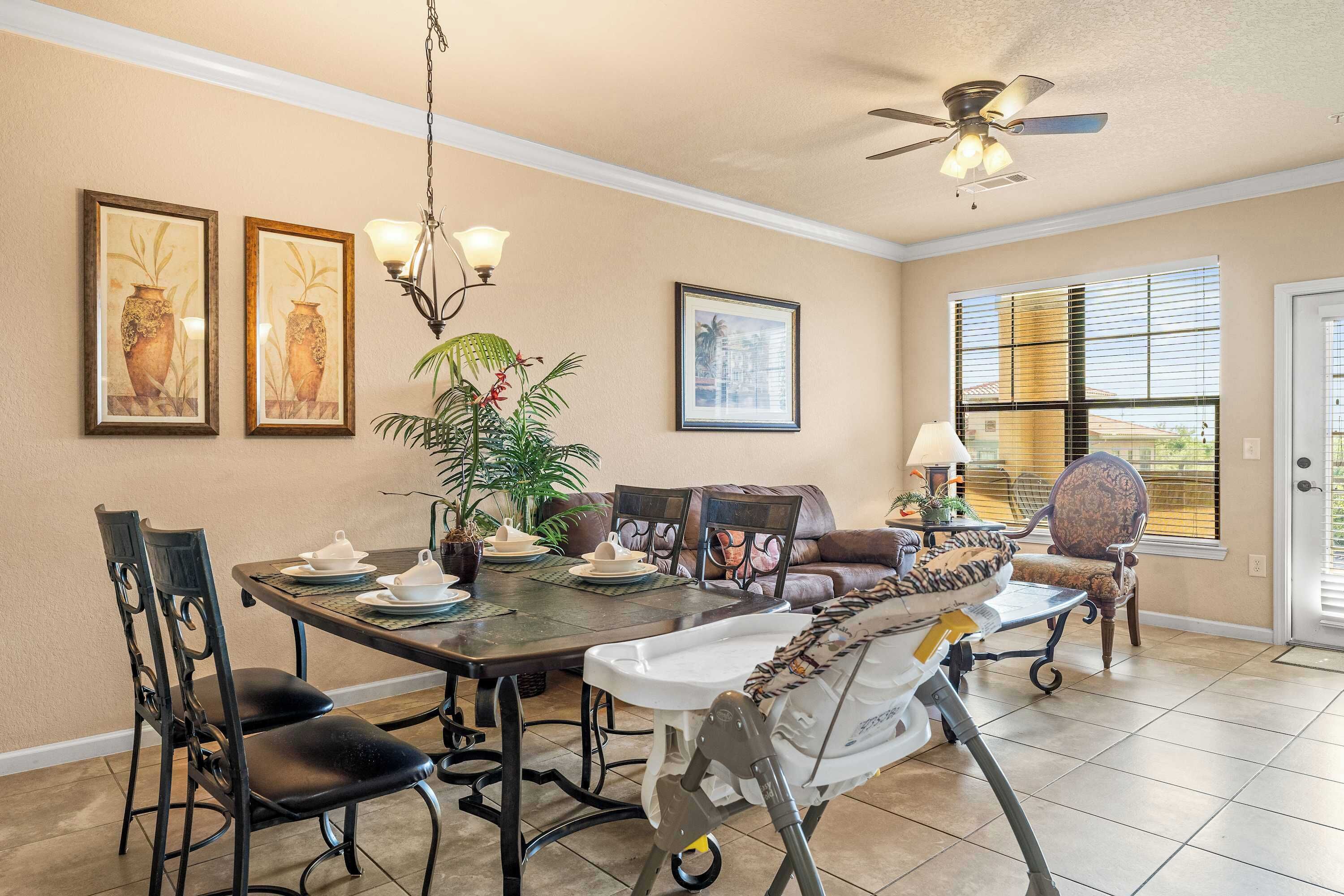 A dining area with a table set for four, surrounded by chairs, a ceiling fan, and framed artwork on the walls.
