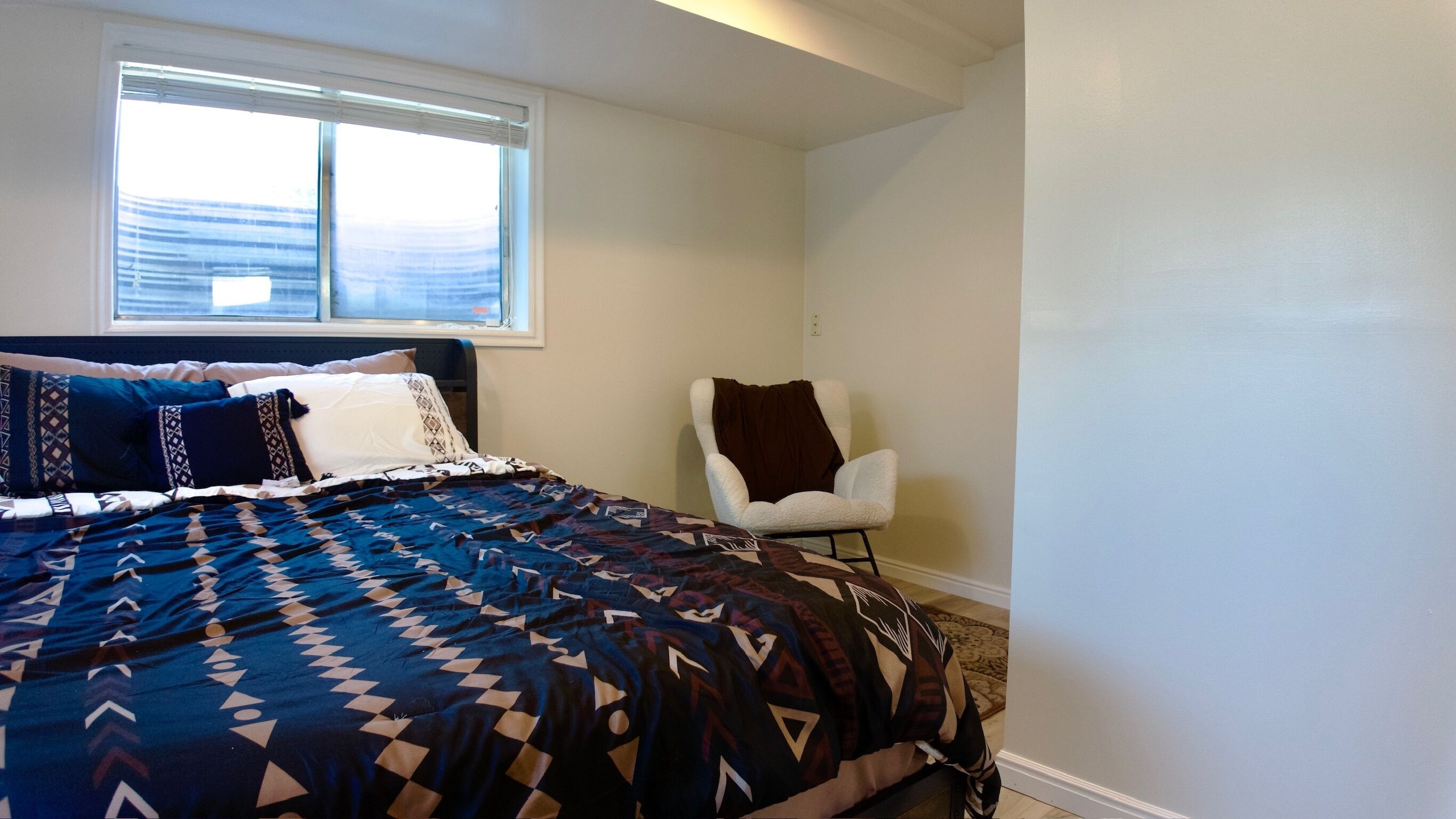 A bedroom with a bed, a chair, a window, and a carpeted floor.