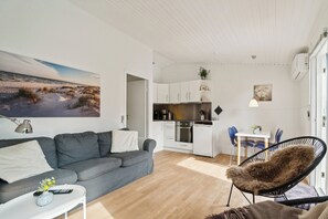 Een moderne woonkamer met een grijze bank, een witte salontafel, een zwarte stoel en een keuken met witte kasten en een eettafel.