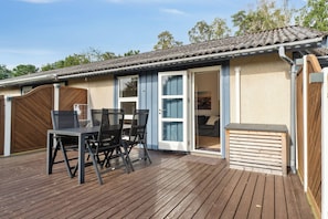 A wooden deck with a table and chairs, a sliding glass door, and a covered outdoor area.