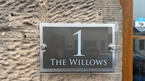 A house number sign with "1" and "The Willows" on a textured stone wall.