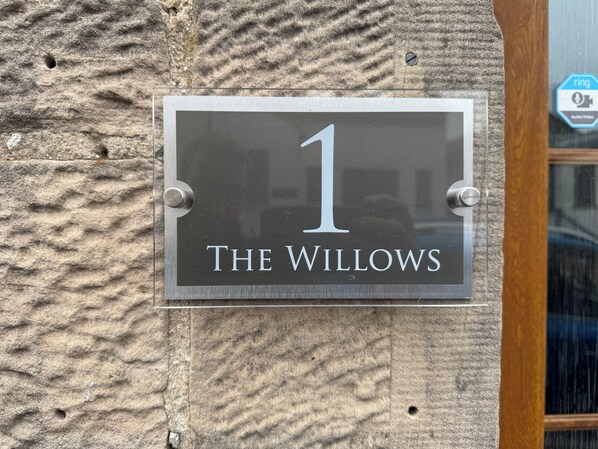 A house number sign with "1" and "The Willows" on a textured stone wall.
