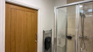 A bathroom with a wooden door, a glass shower enclosure, and a towel rack.