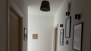 A hallway with a wooden door, a black pendant light, and framed pictures on the walls.