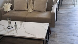 A modern bedroom with a sofa bed, a marble coffee table, and a bedside table with a lamp.
