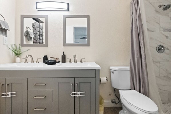 Une salle de bain avec un lavabo blanc, des meubles gris, des toilettes et un rideau de douche.