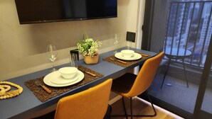 A dining table set with white plates, bowls, and cutlery, accompanied by a small potted plant and a woven placemat.