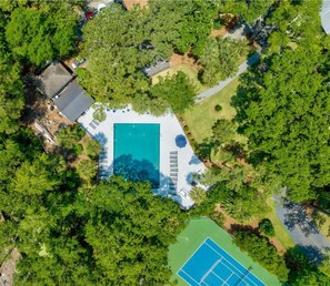 Vista aèria d'una propietat amb piscina, pistes de tennis i un edifici petit, tot envoltat d'arbres.