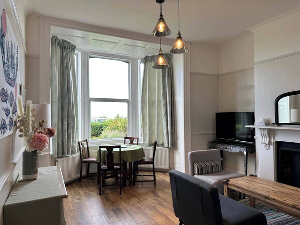 A dining area with a table and chairs, a fireplace, a television, and a window with curtains.