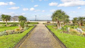 A pathway leading to a beach area with palm trees and a gazebo. - Stunning 1-bed Flat W/seaview, Garden Pet Friendly (Herne Bay)