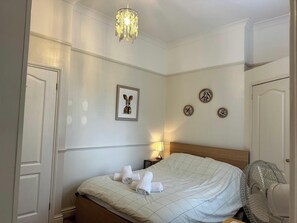 A neatly made bed with rolled towels, a chandelier, wall clocks, and a framed artwork.