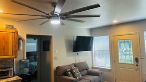 A living room with a ceiling fan, a television, a water dispenser, a couch, and a door with a window. - Adorable 2 Bedroom Unit with Boat Parking (Dauphin Island)